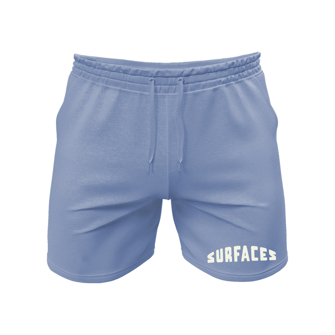 Blue shorts with a drawstring and an embroidered logo on the bottom of the left leg that reads "Surfaces".